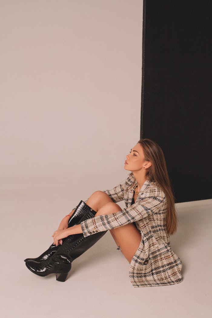 services-01 Stylish woman with long hair sitting indoors in boots and coat, side view.